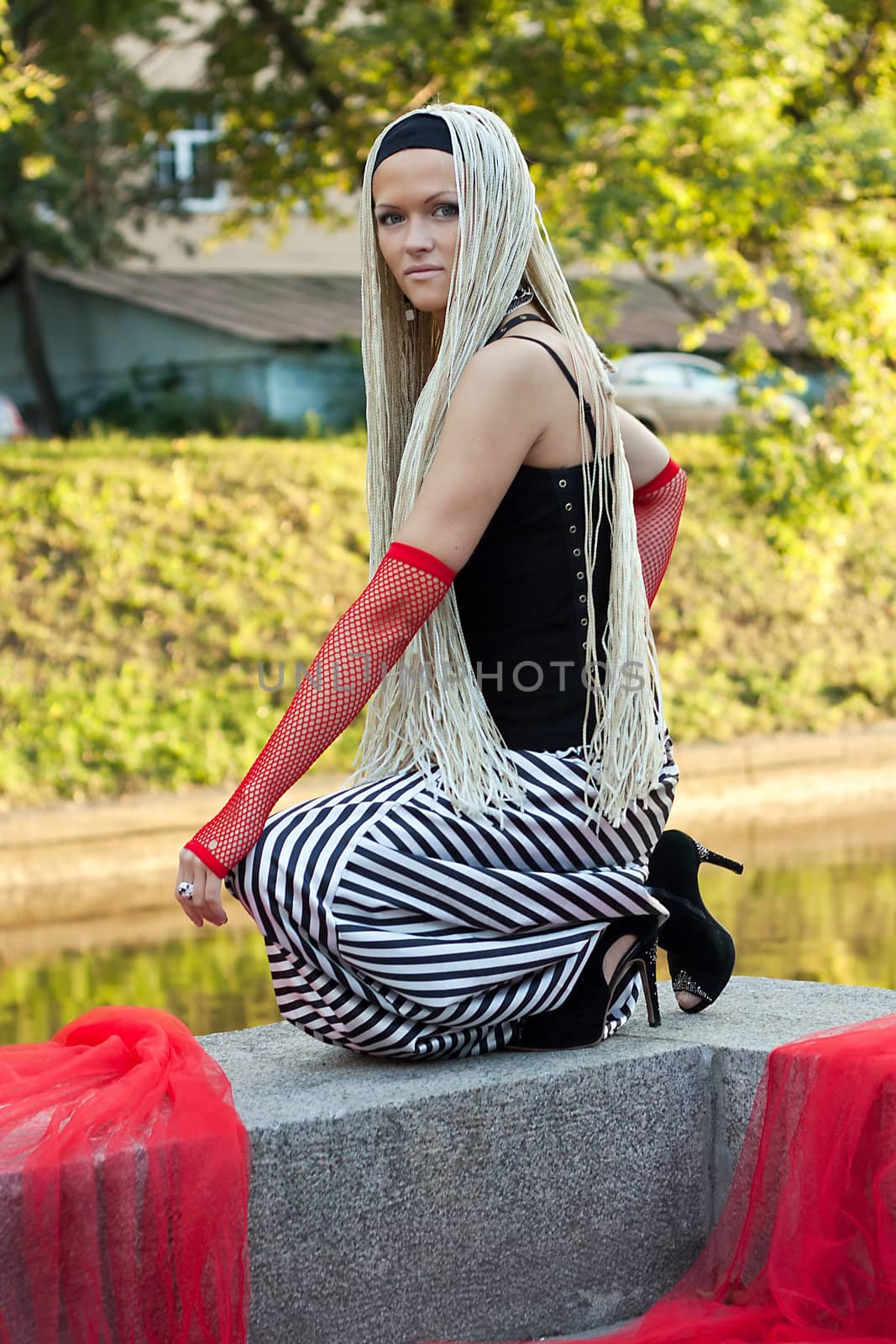 Young woman with braided seating near the river. On her hands are red gloves