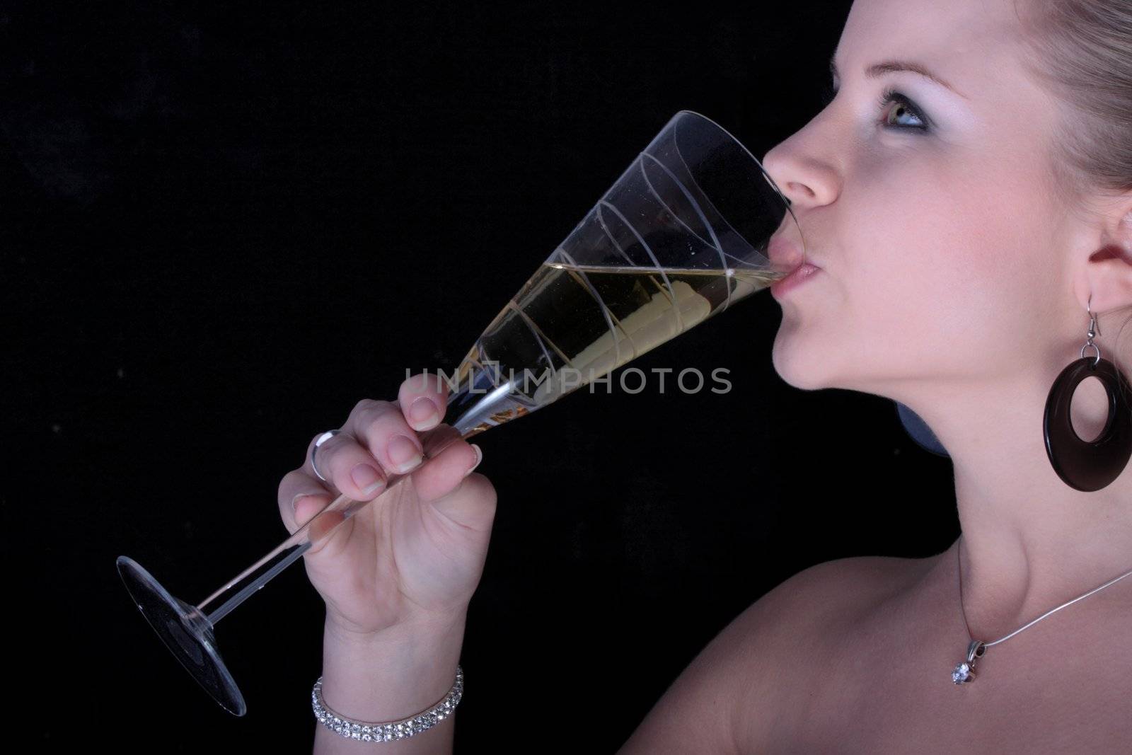 Beautiful blonde drinking a champagne from glass on black background.