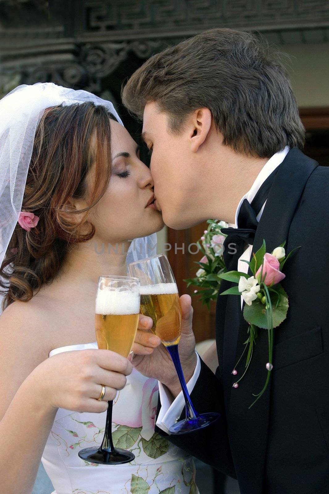 Half body portrait of young adult newlywed couple kissing and toasting each other with drinks.