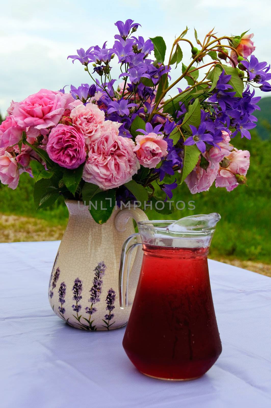 A flower bouquet and a mug with red juice out in the garden