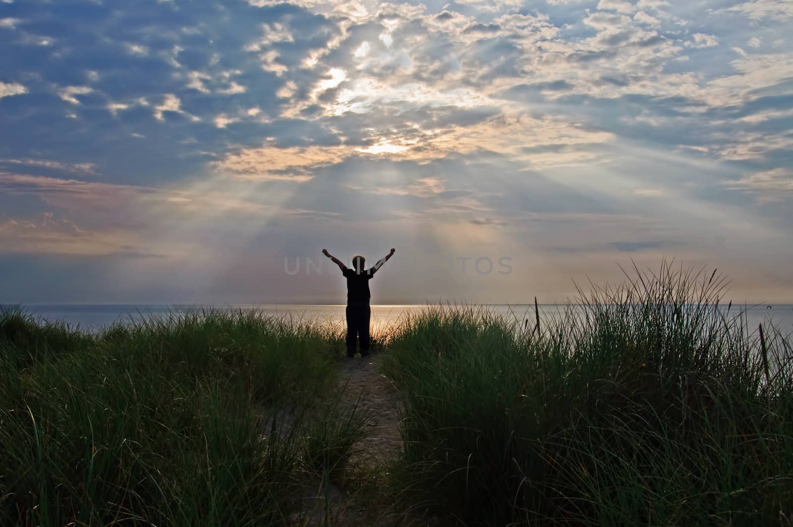 A person is standing on top of dunes greeting the sun