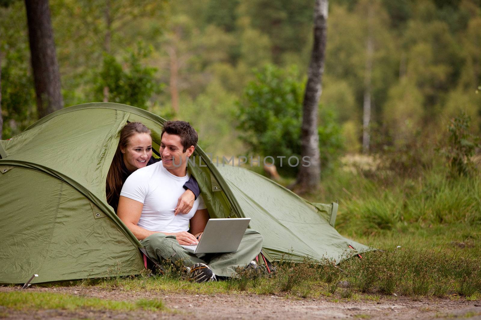 A couple using a computer outside a tent on a camping trip