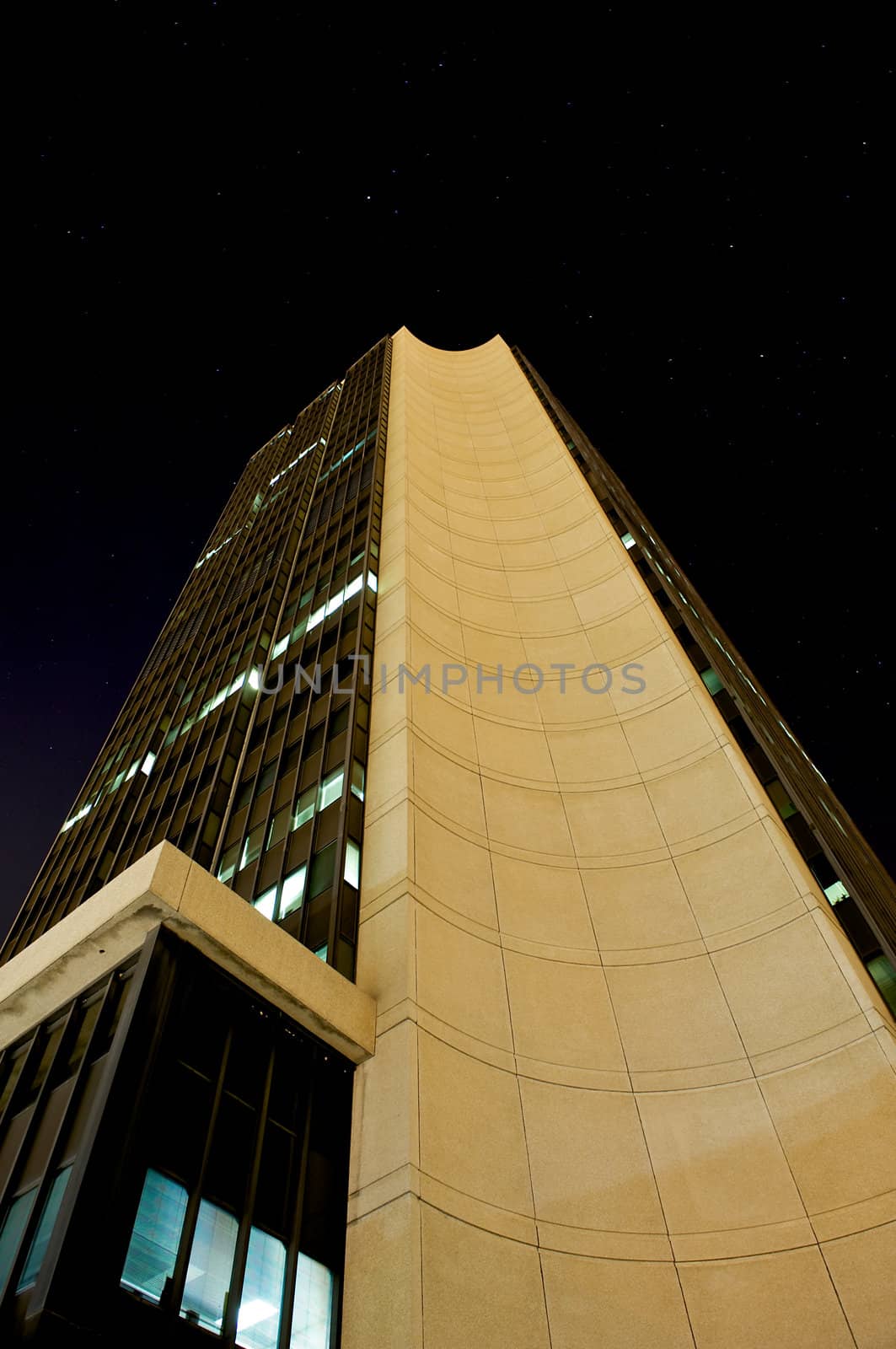 Tall business building at night showing many windows still illuminated, illustrating the late hours put in by many business men to get the job done.