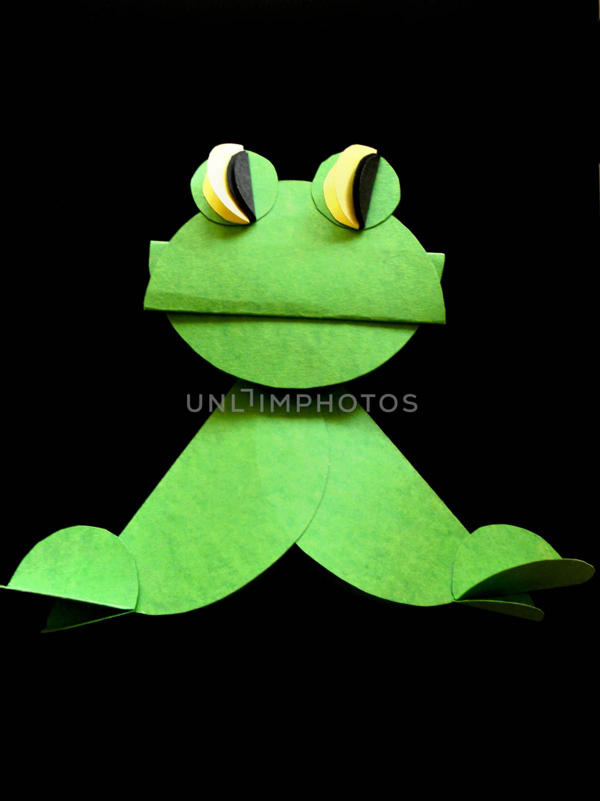 One green frog made from paper on the black background.