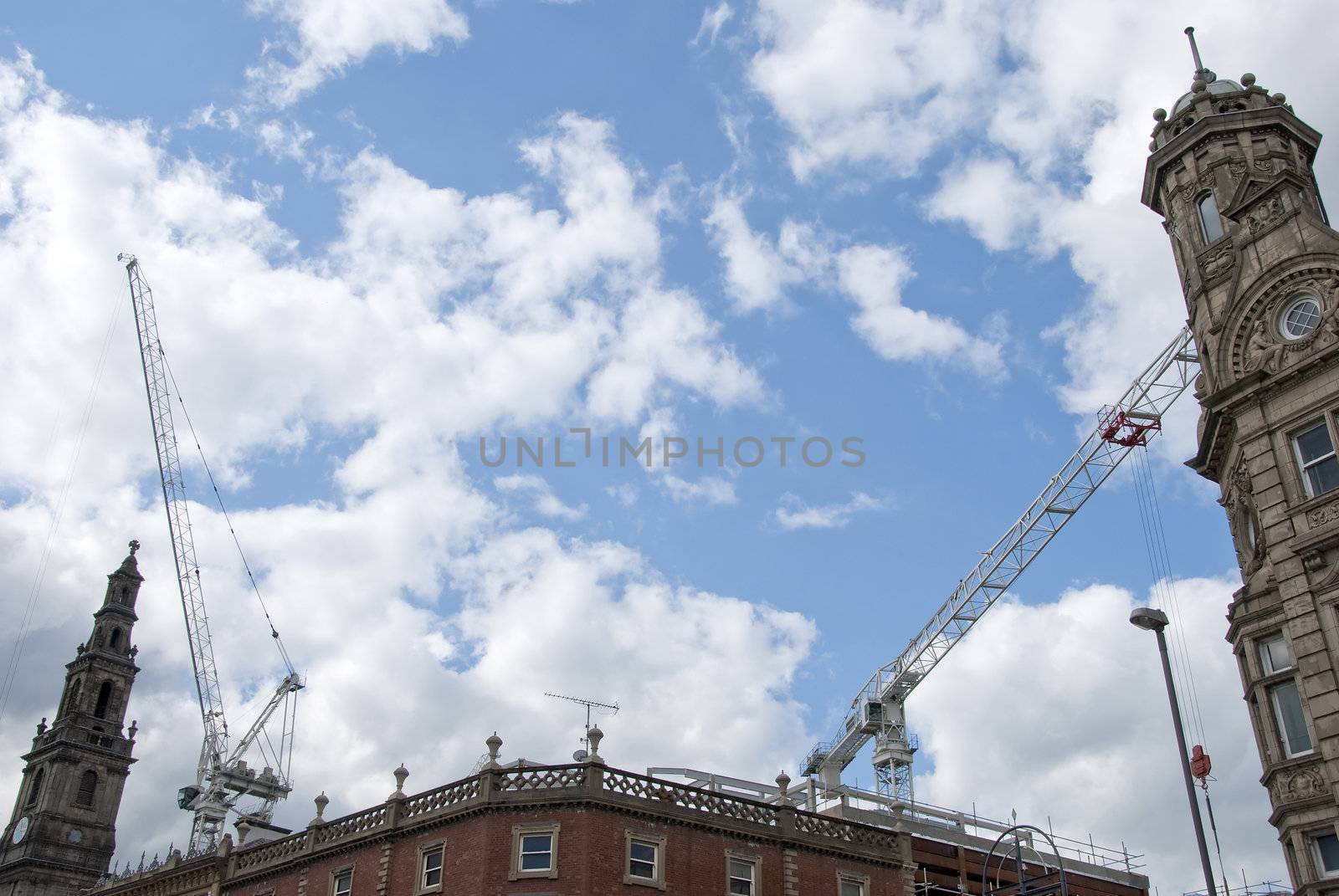 Two construction cranes and an old clocktower in an english city