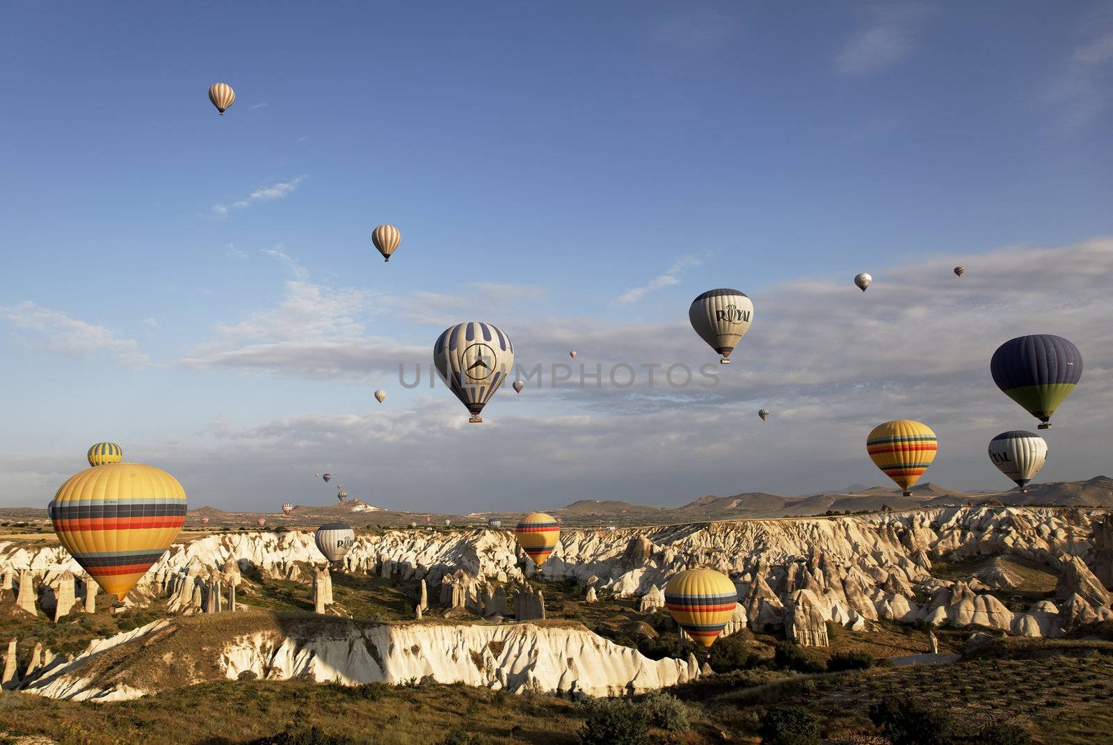 Cappadocia, Turkey: June 2011 - skies over Kapadokya filled with colorful hot air balloons, blue sky, wispy clouds, mountain landscape and rough terrain