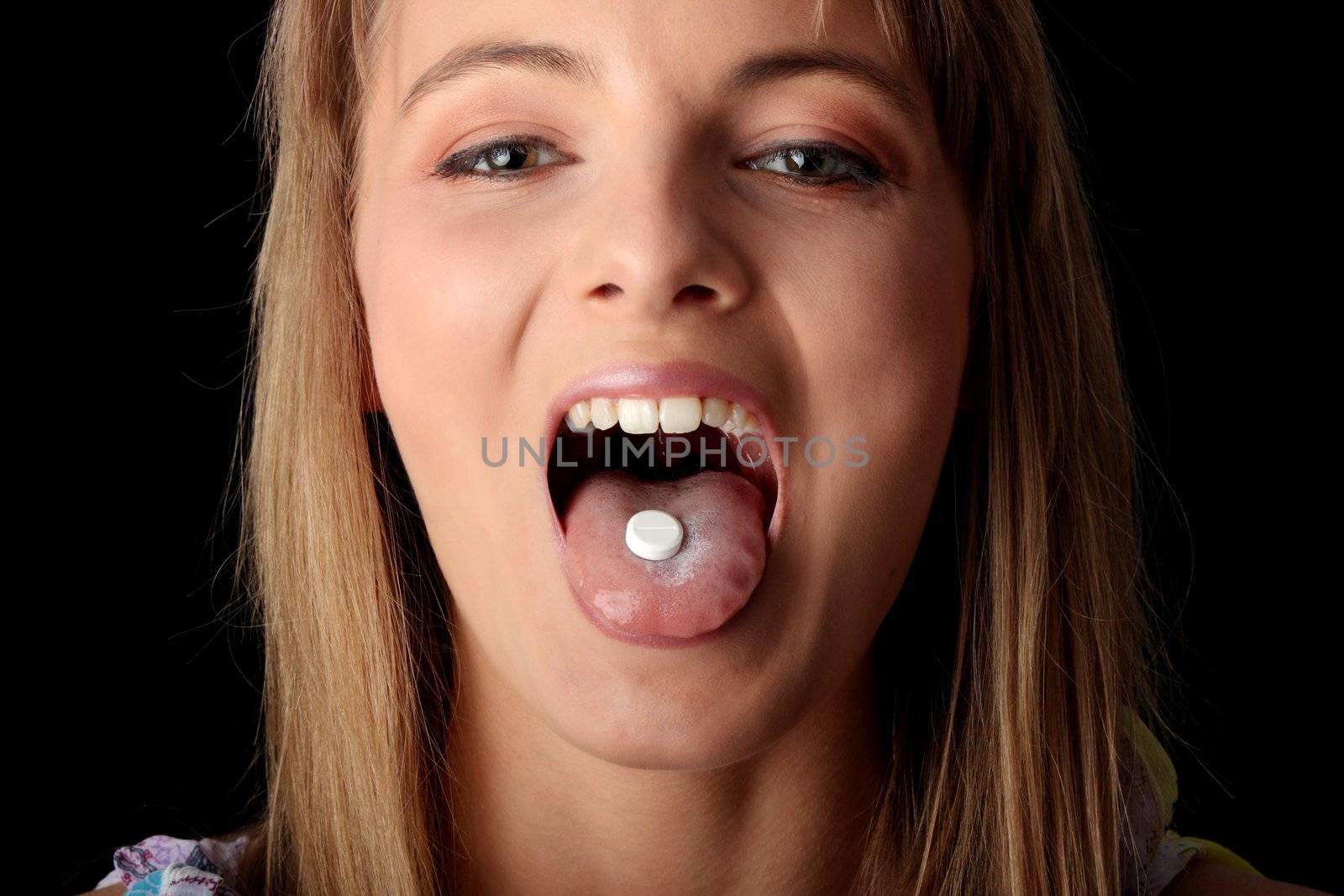Young woman eating a pill isolated on black background