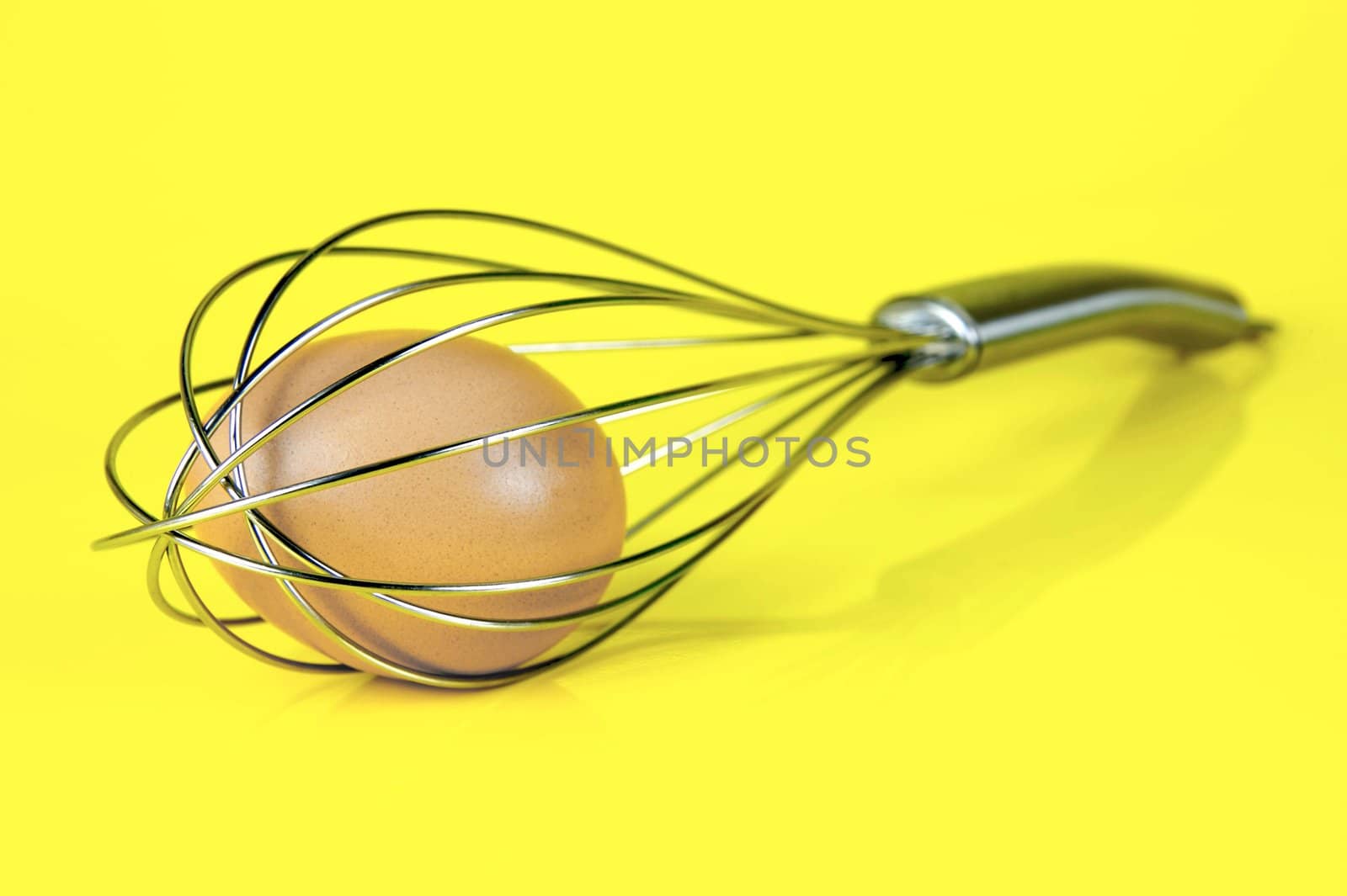 An egg and and a egg beater together isolated against a yellow background