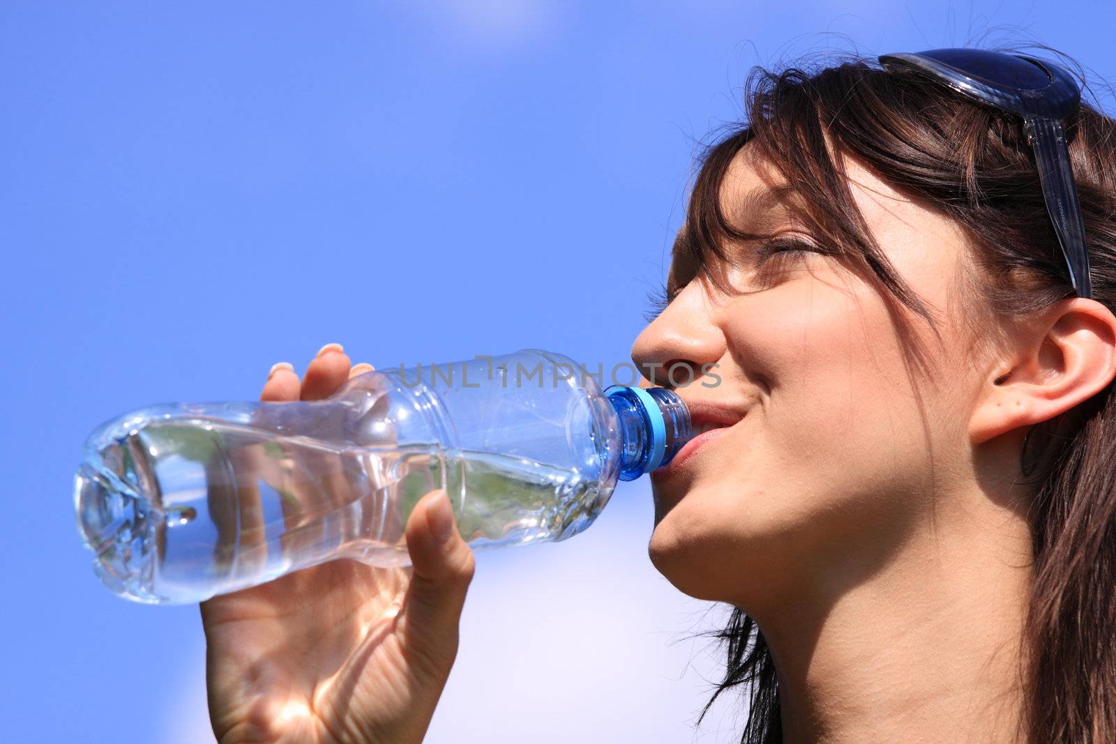 Girl drinking water against blue sky in sunny day