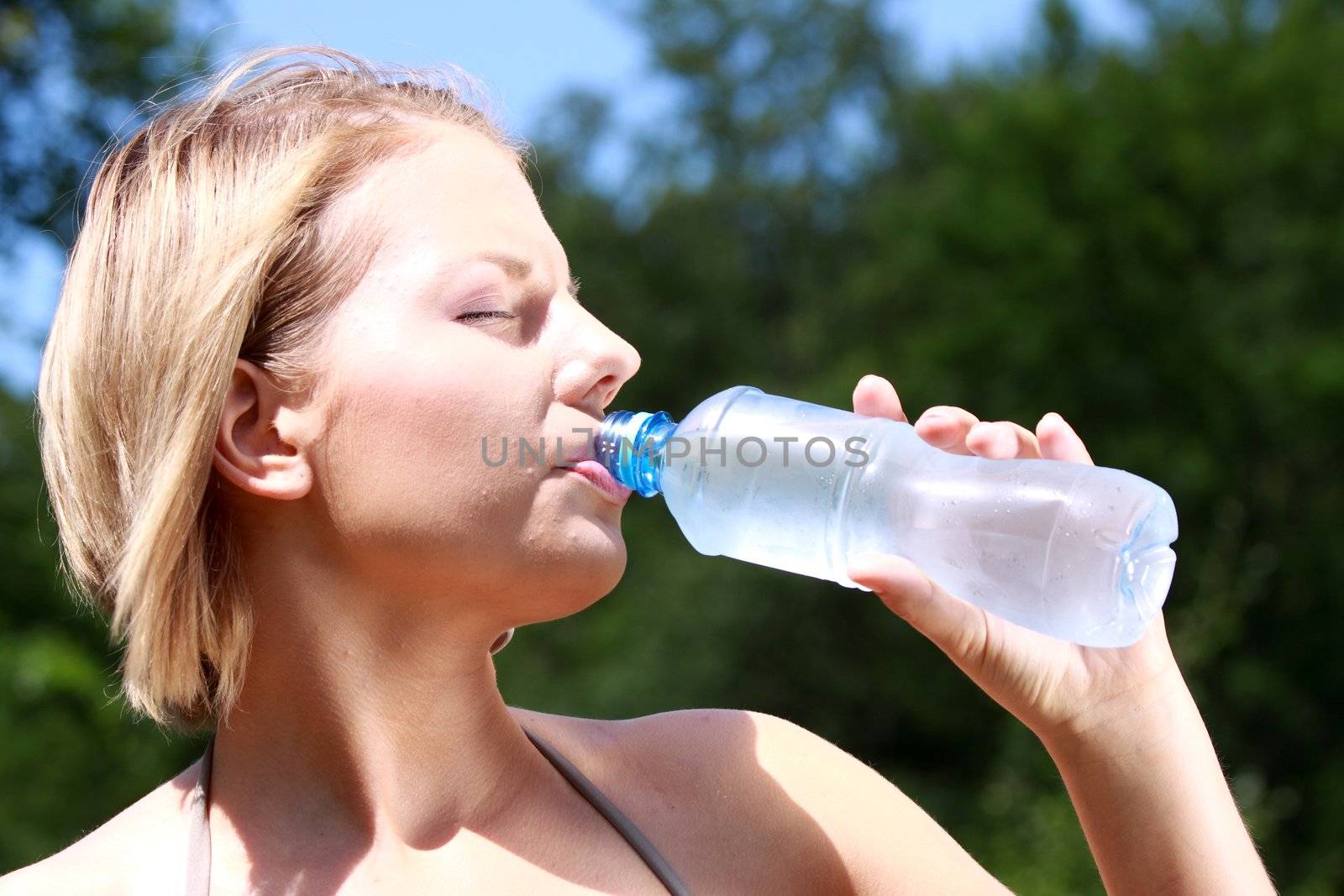 Pretty woman drinking water on the summer glade