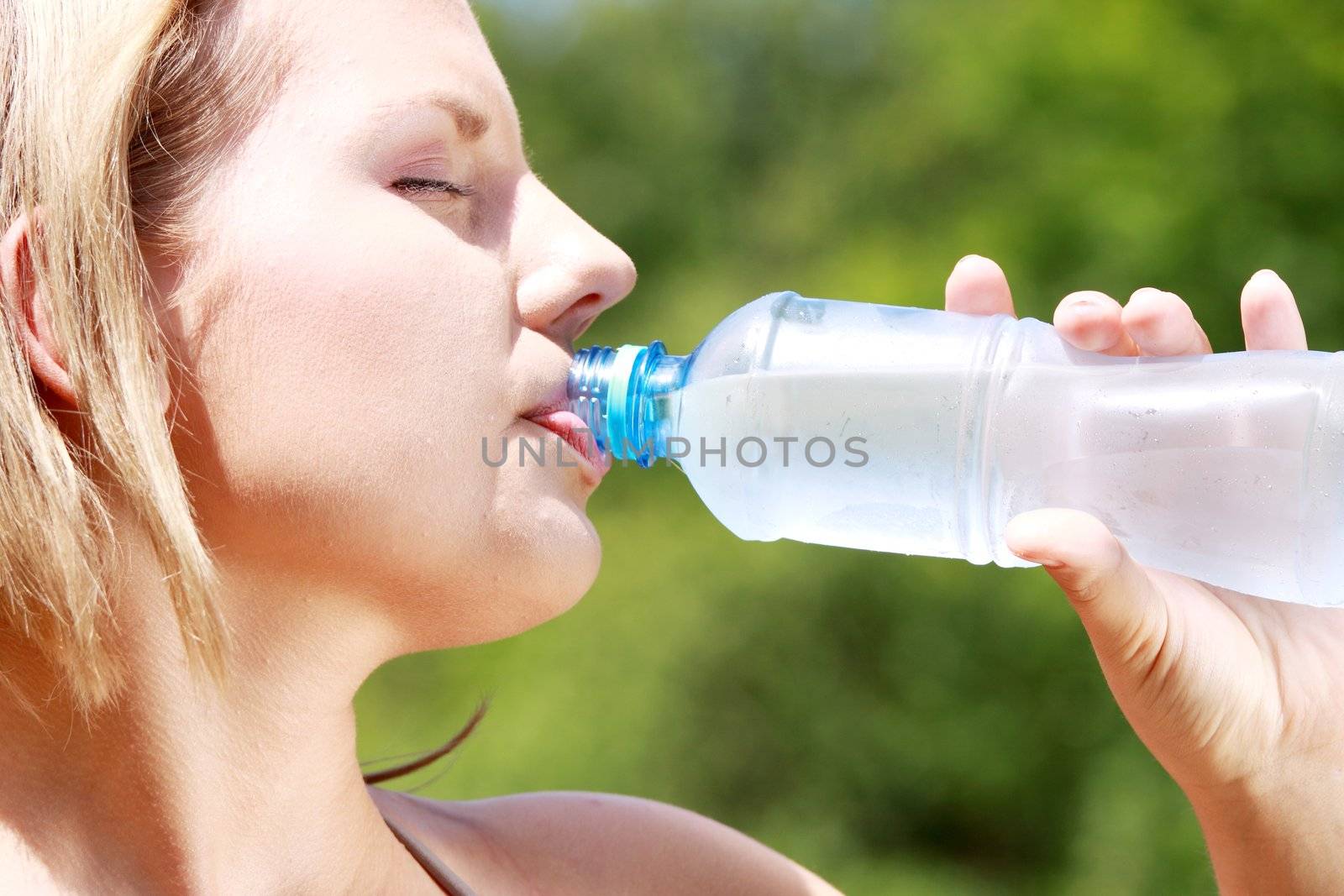 Pretty woman drinking water on the summer glade