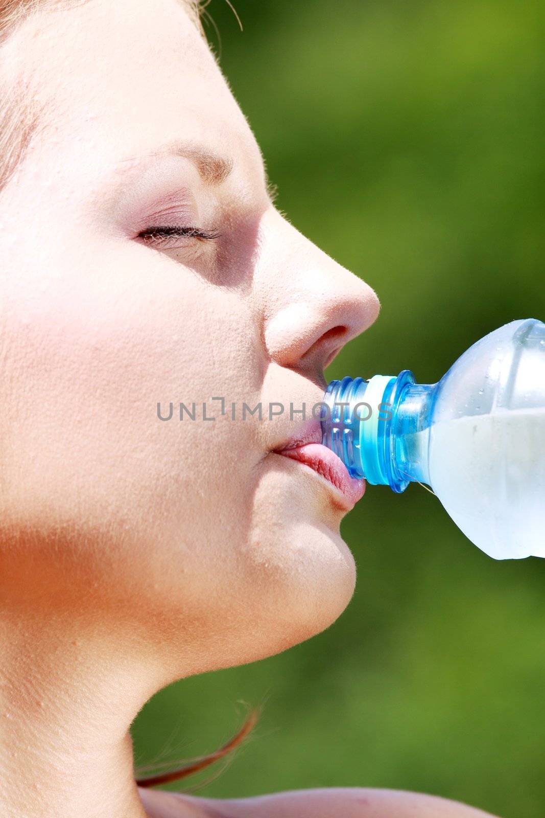 Pretty woman drinking water on the summer glade
