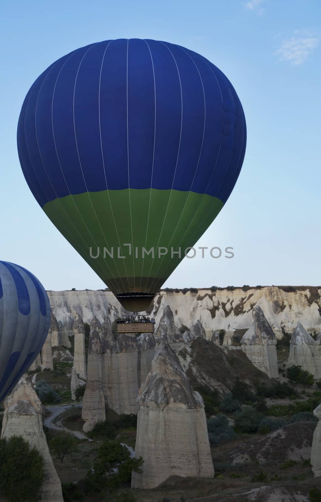 Green Blue hot air balloon low level flight over chimney peaks Cappadocia, blue sky, lava ash layered hils, portrait, copy space, crop space