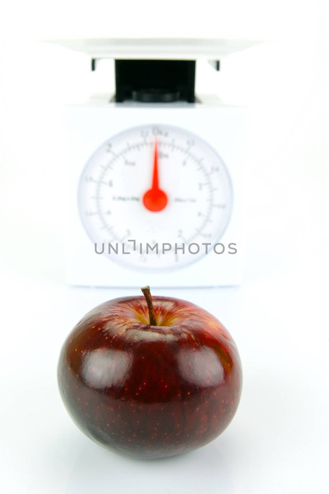 A red apple on top of a set of kitchen scales isolated against a white background