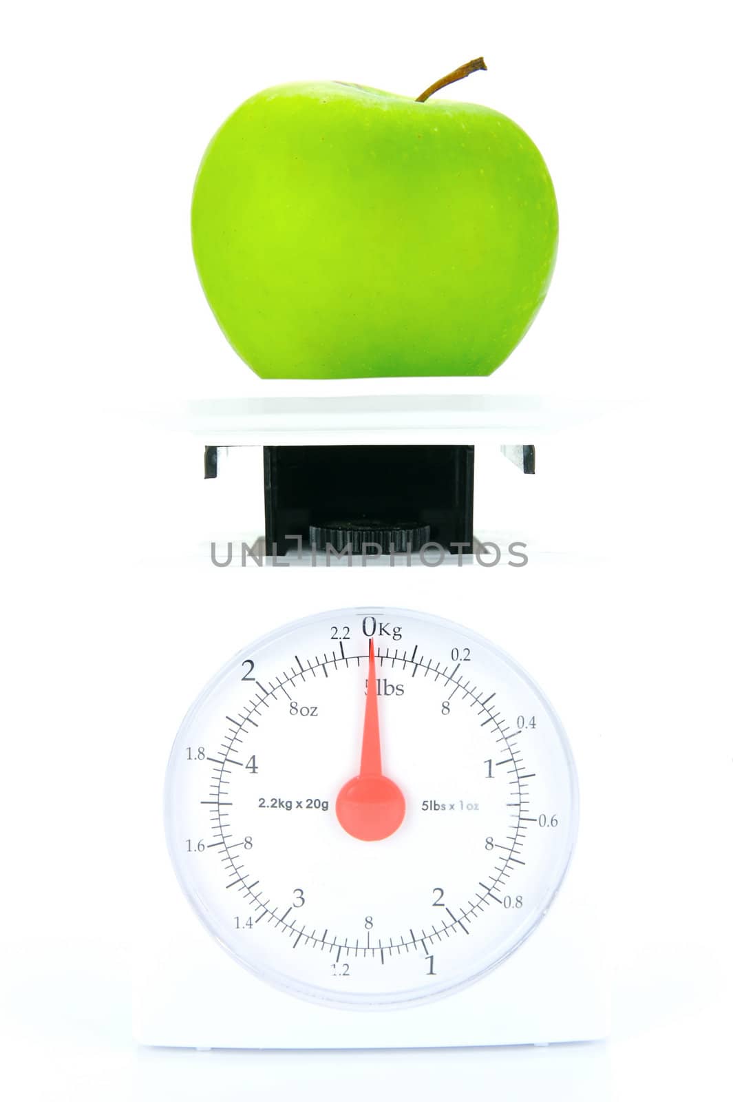 A green apple on top of a set of kitchen scales isolated against a white background