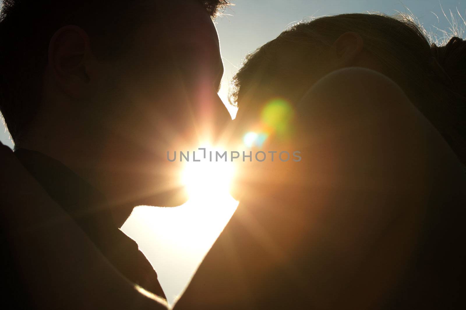 Silhouette of a young couple kissing with the sun setting behind them
