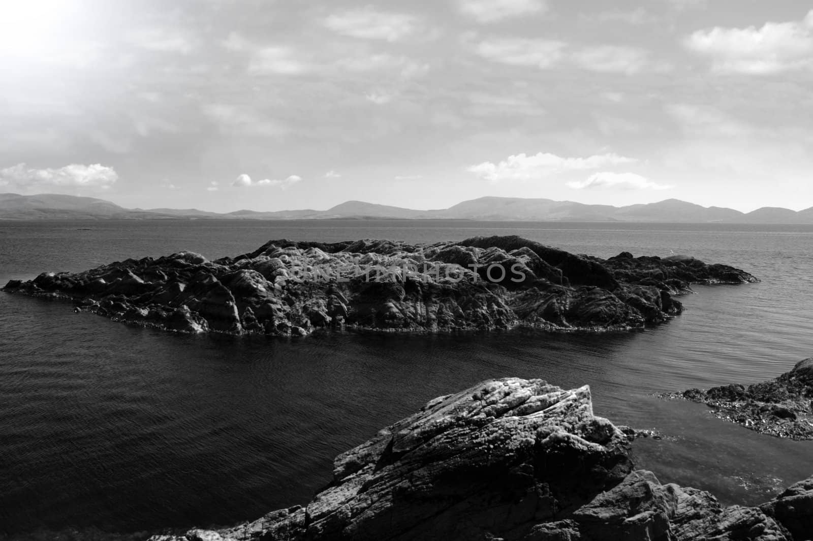 scenic view in kerry ireland of rocks and sea with mountains against a beautiful cloudy sky in black and white