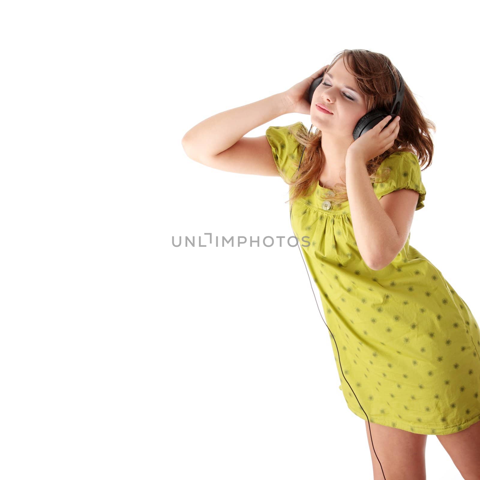 Beautiful teenage girl in a green dress listening to music with big headphones, isolated on white