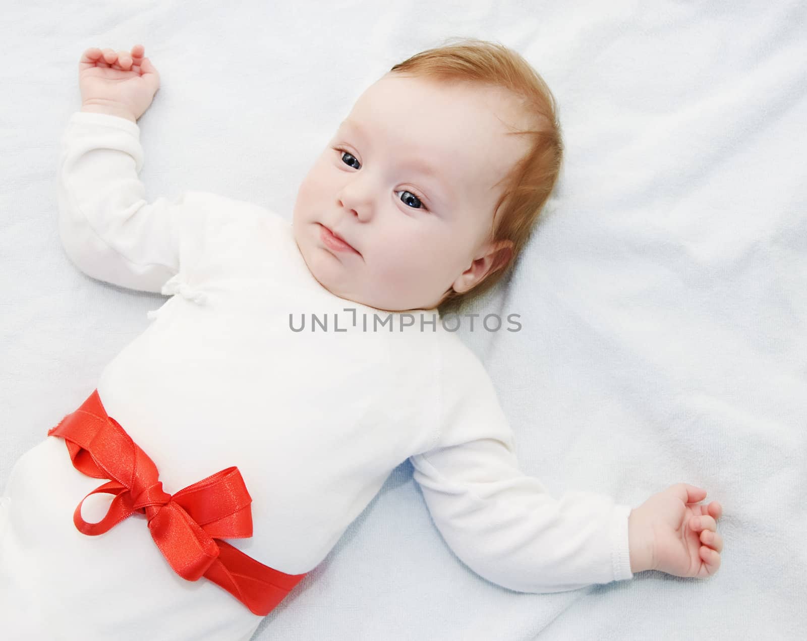 Adorable baby boy in light with red ribbon as gift