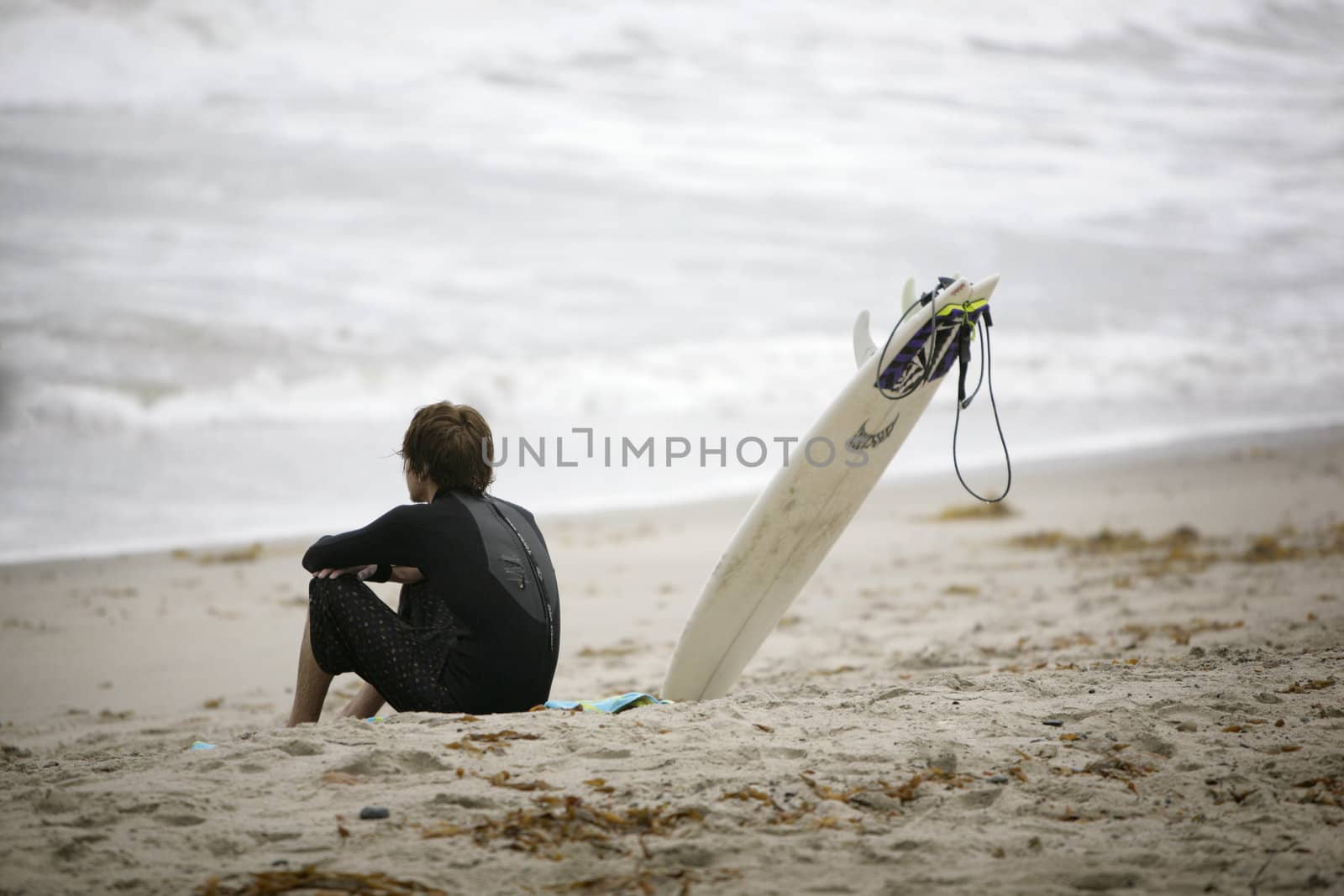 young surfer sitting on the beach and watching the waves