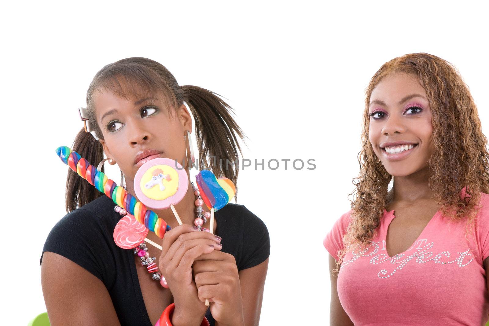 Two pretty black girls sitting next to each other; one is having candy but looking very unhappy, while the other is beaming