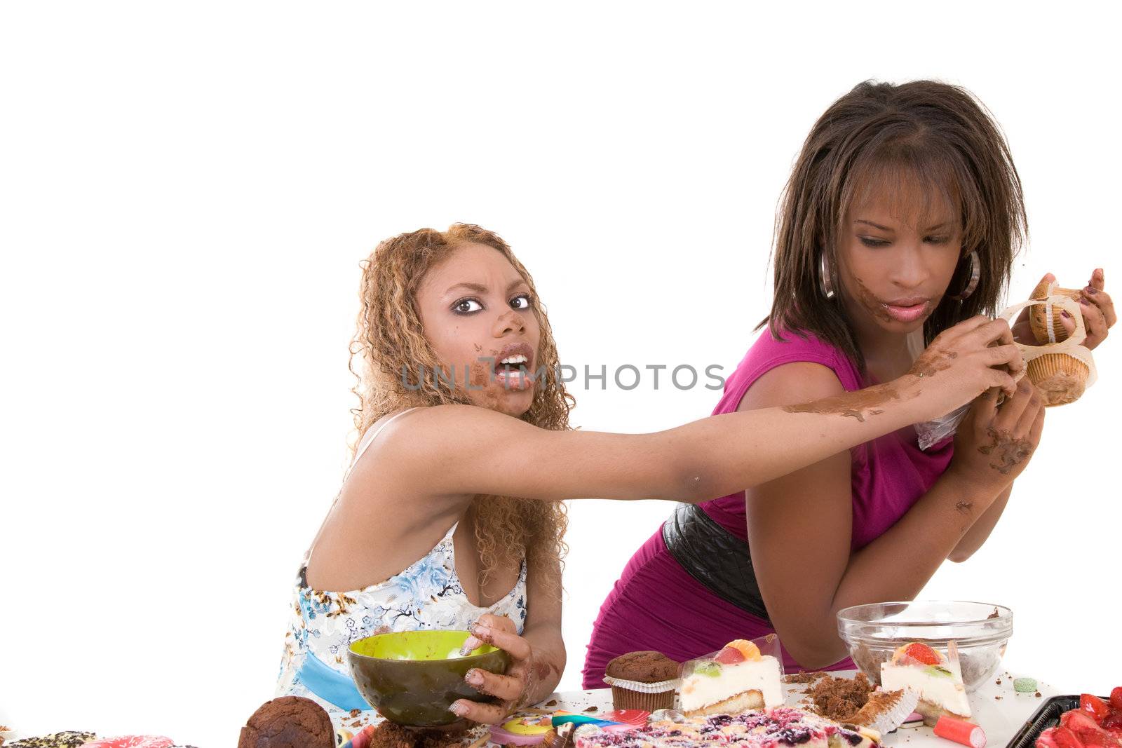 Two black girls fighting over a bunch of muffins while the entire table in front of them is loaded with food