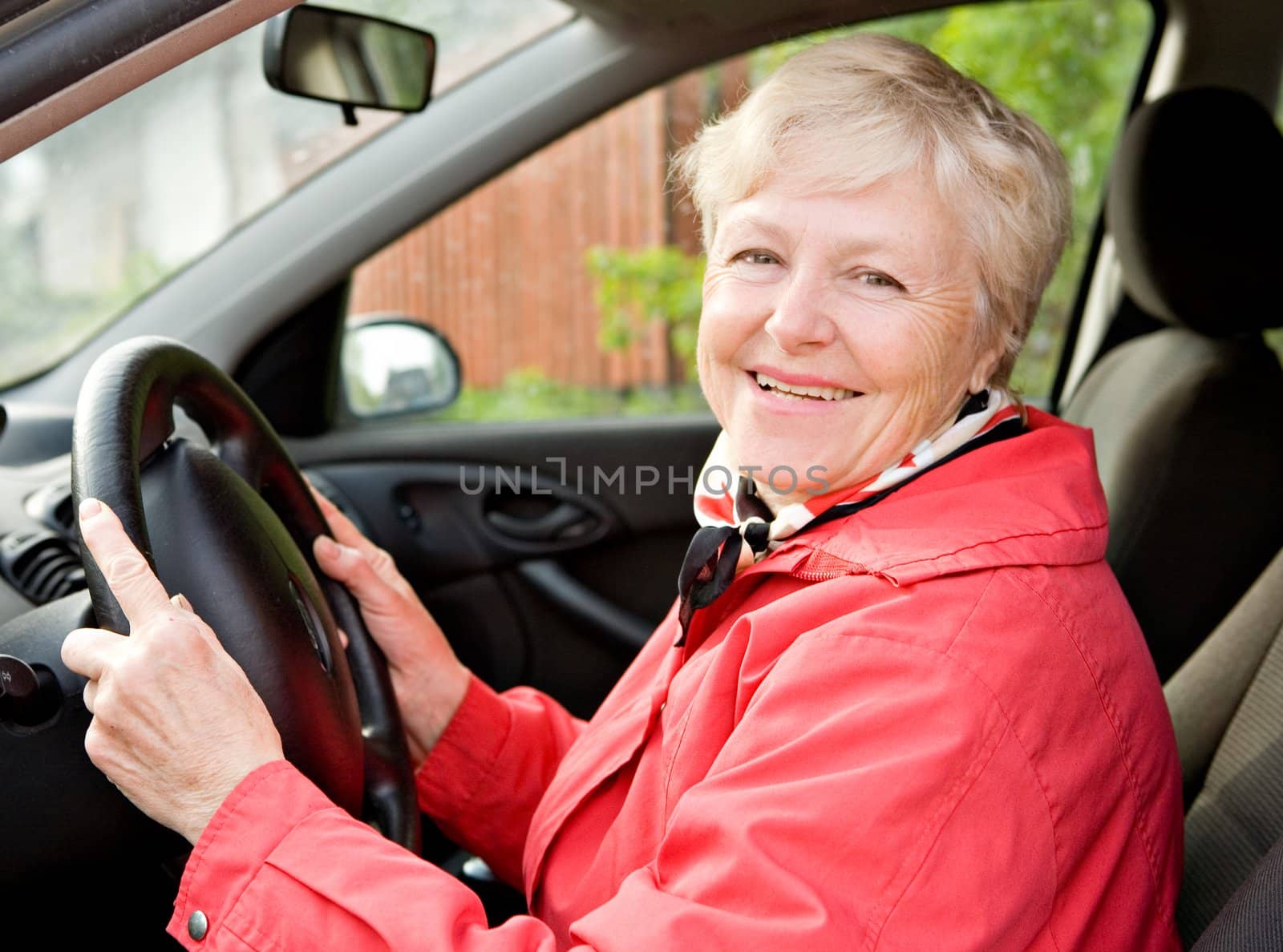 The smiling elderly woman in a red jacket at the wheel the car
