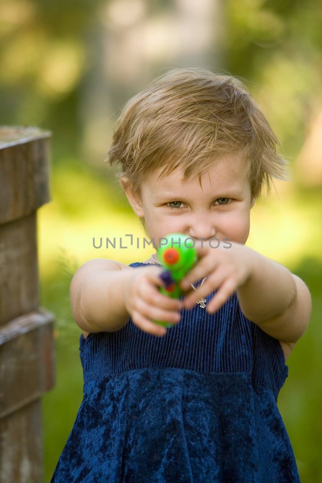 The little girl in a dark blue dress is going to shoot from a water pistol in summer day
