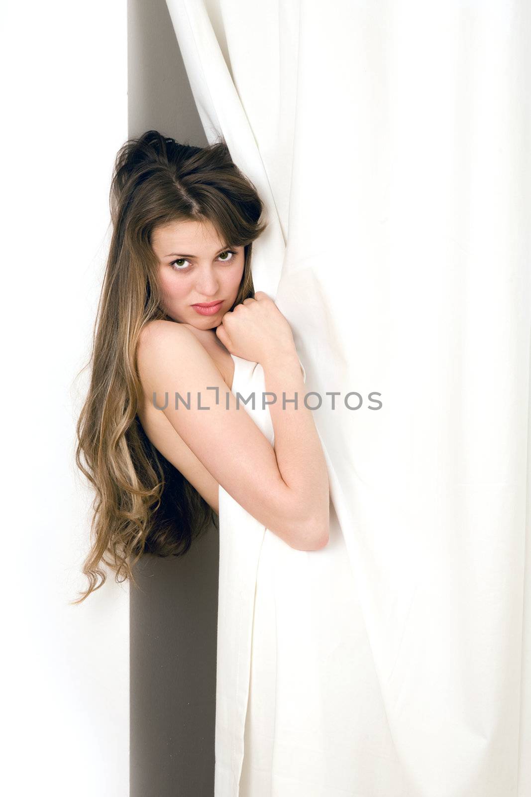 Beautiful young woman looking from behind a white curtain