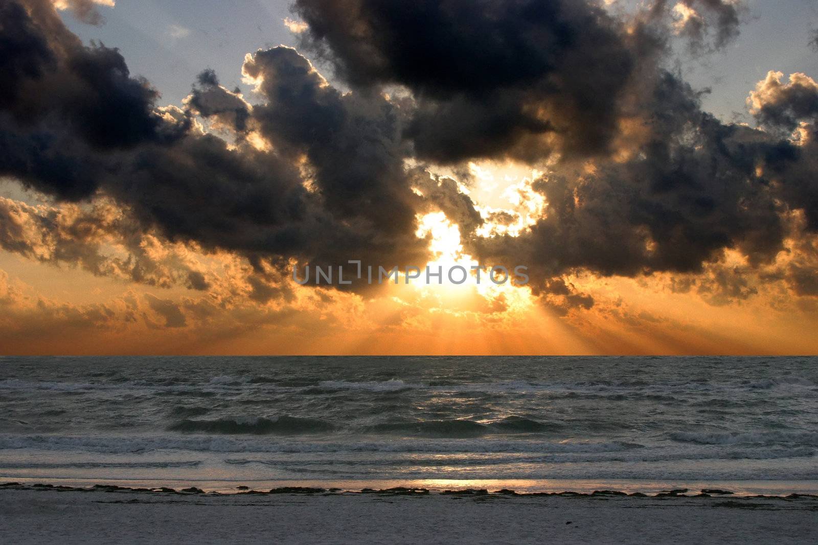 Powerful clouds tower over the shoreline while sun rays beam through the clouds in dramatic fashion.