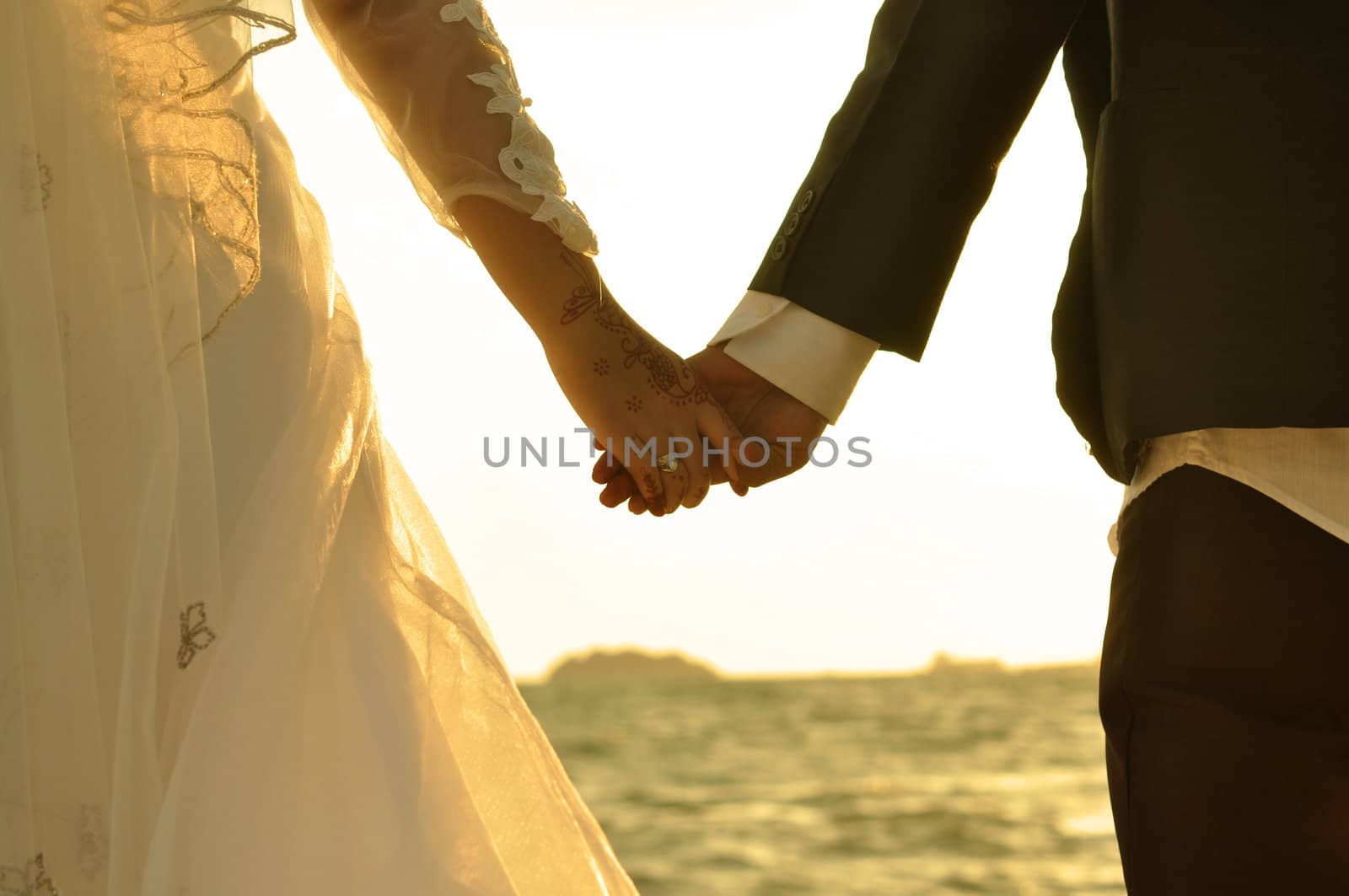 Young adult male groom and female bride holding hands on beach at sunset.