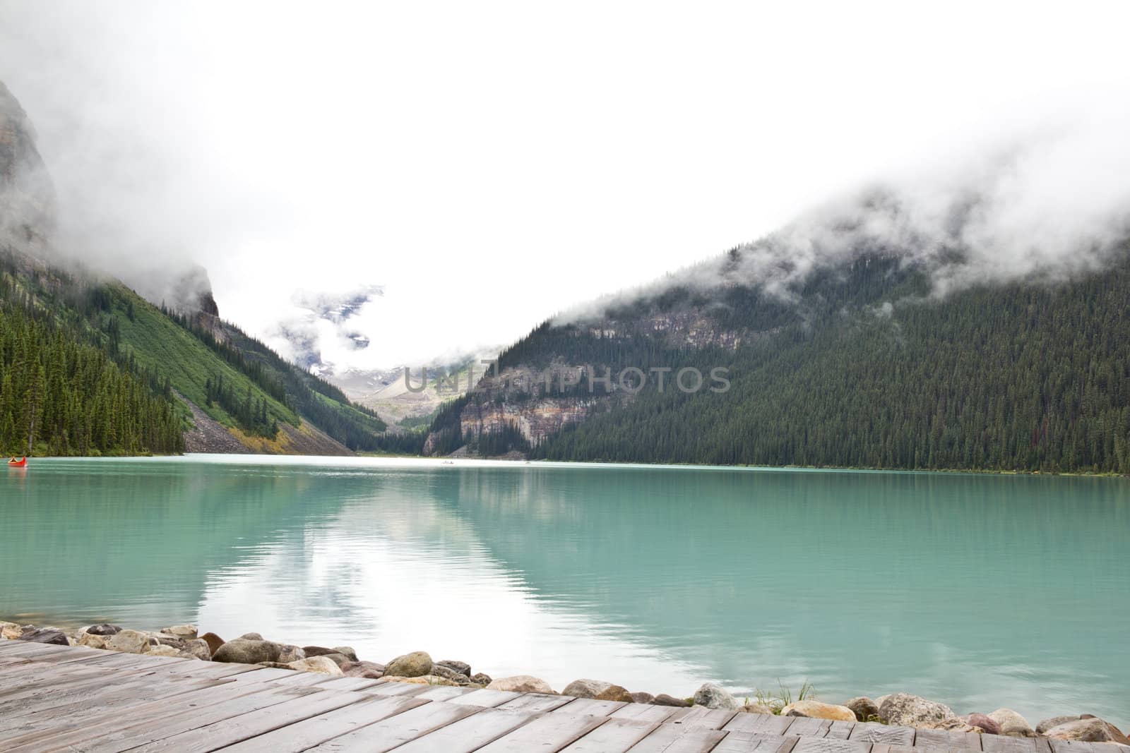 The beautiful turquoise colored Lake Louis against the backdrop of the majestic mountains of the Canadian Rockies partially covered with fog