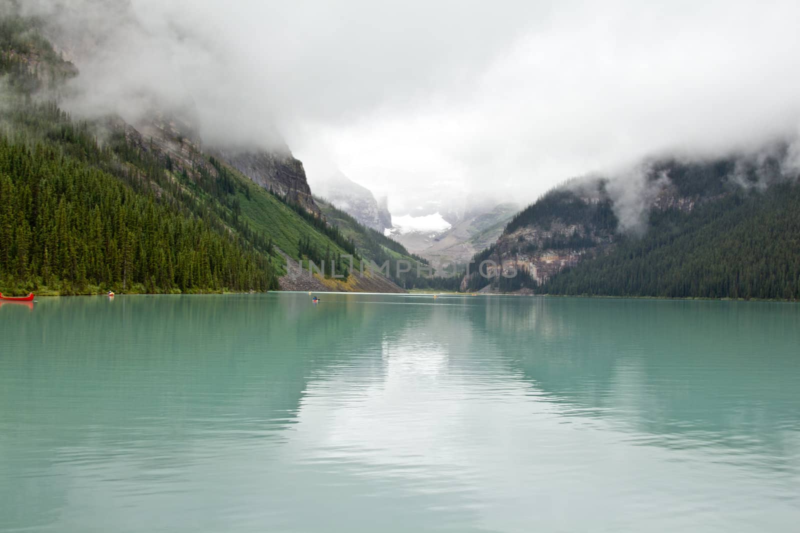 The beautiful turquoise colored Lake Louis against the backdrop of the majestic mountains of the Canadian Rockies partially covered with fog