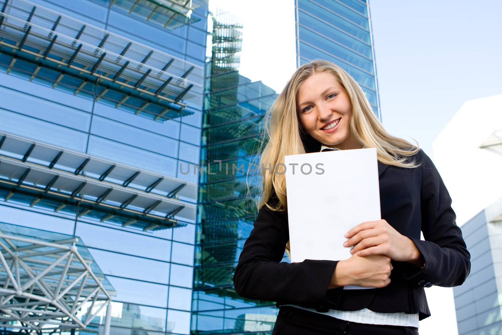 Blonde business woman posing in front of a modern blue office building