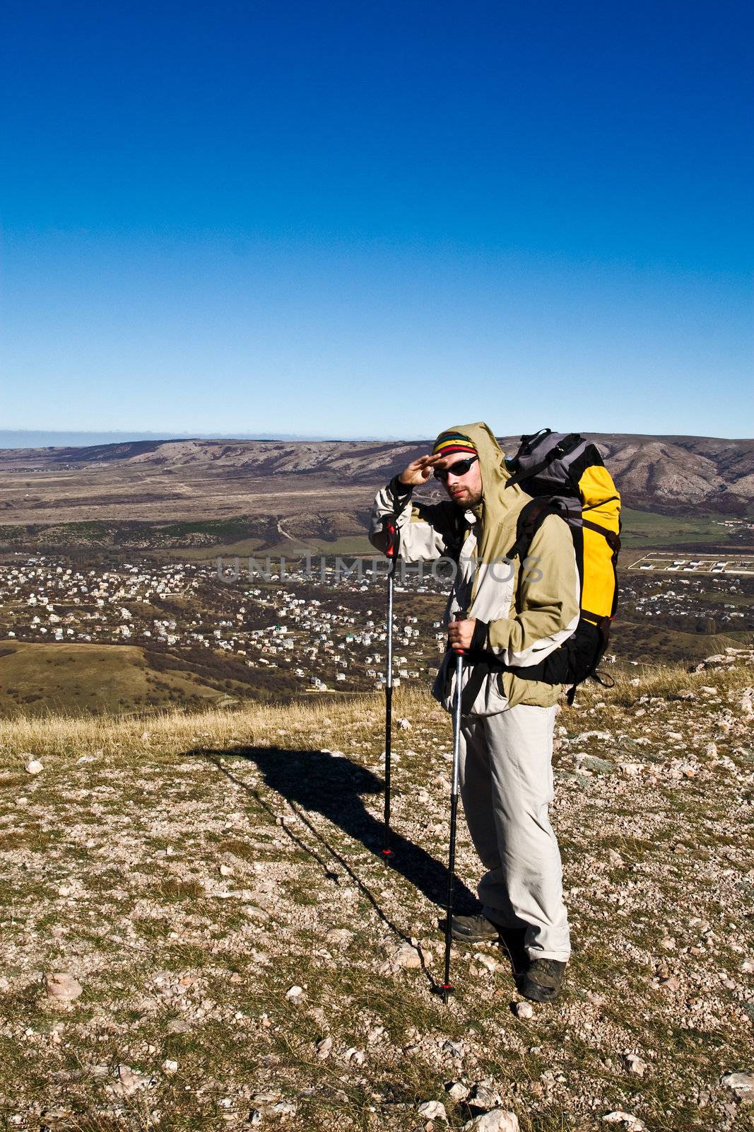 Hiker in sunglasses and with hiking poles on mountain summit looking ahead
