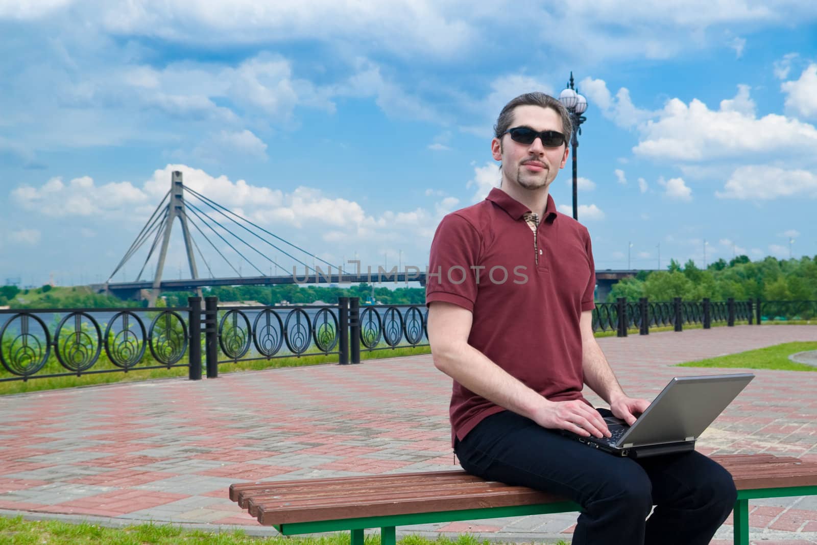 Young man sitting on a park bench with his laptop