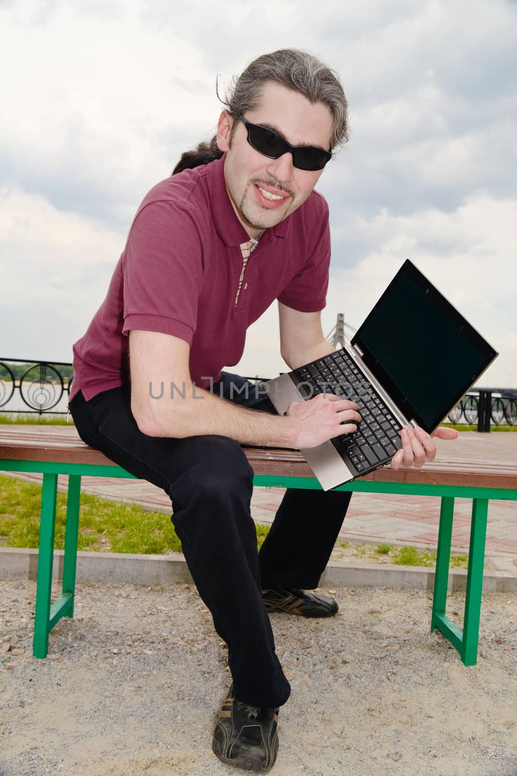 Young man sitting on a park bench with his laptop