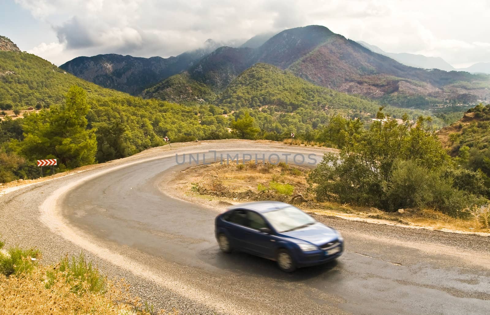 Dark blue car goes up the serpentine road in mountains in cloudy weather