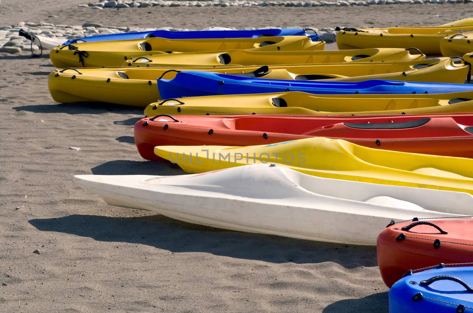 Bright white, yellow, red and blue canoes lie on sandy beach