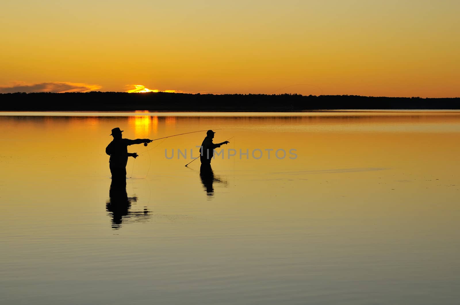 Fishermen silhouettes at dusk fishing in a lake