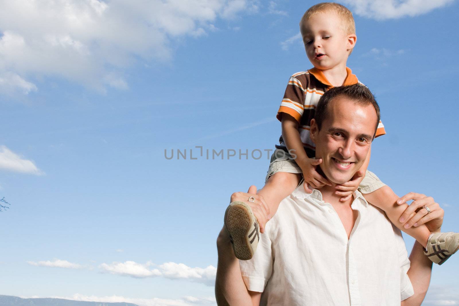 Father carrying his son on piggy back ride outdoors against nature and blue sky