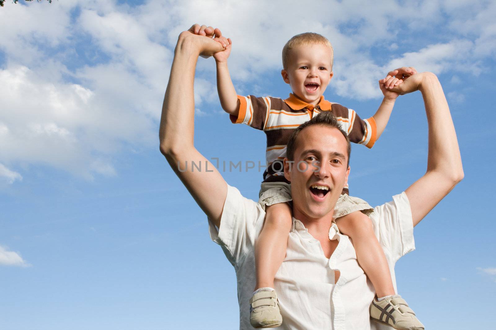 Father carrying his son on piggy back ride outdoors against nature and blue sky