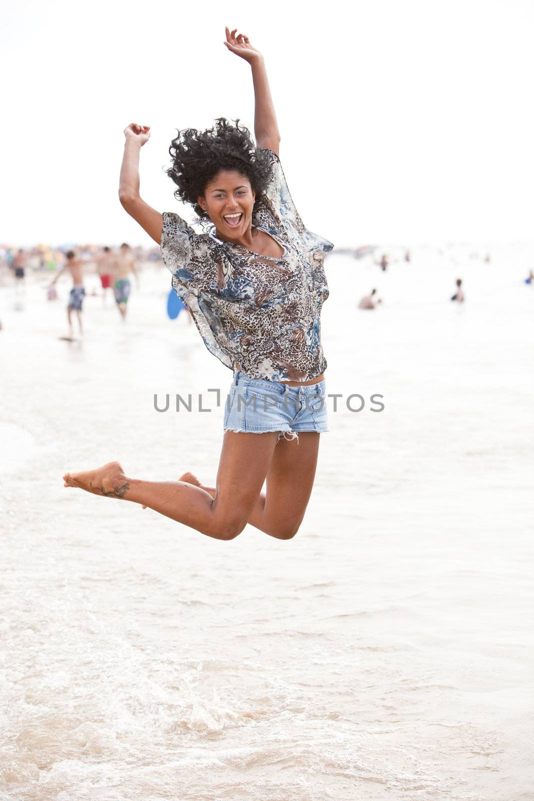 Beautiful brazilian girl jumping up from the water at the beach