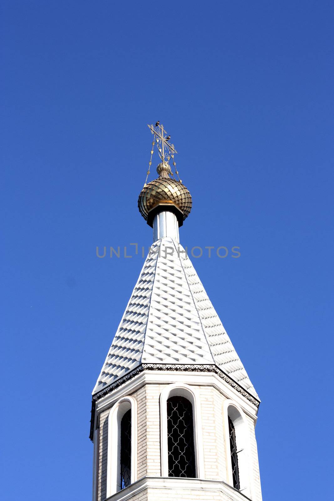 Golden dome of the Orthodox church in Central Russia on the blue sky background partially covered with snow. 