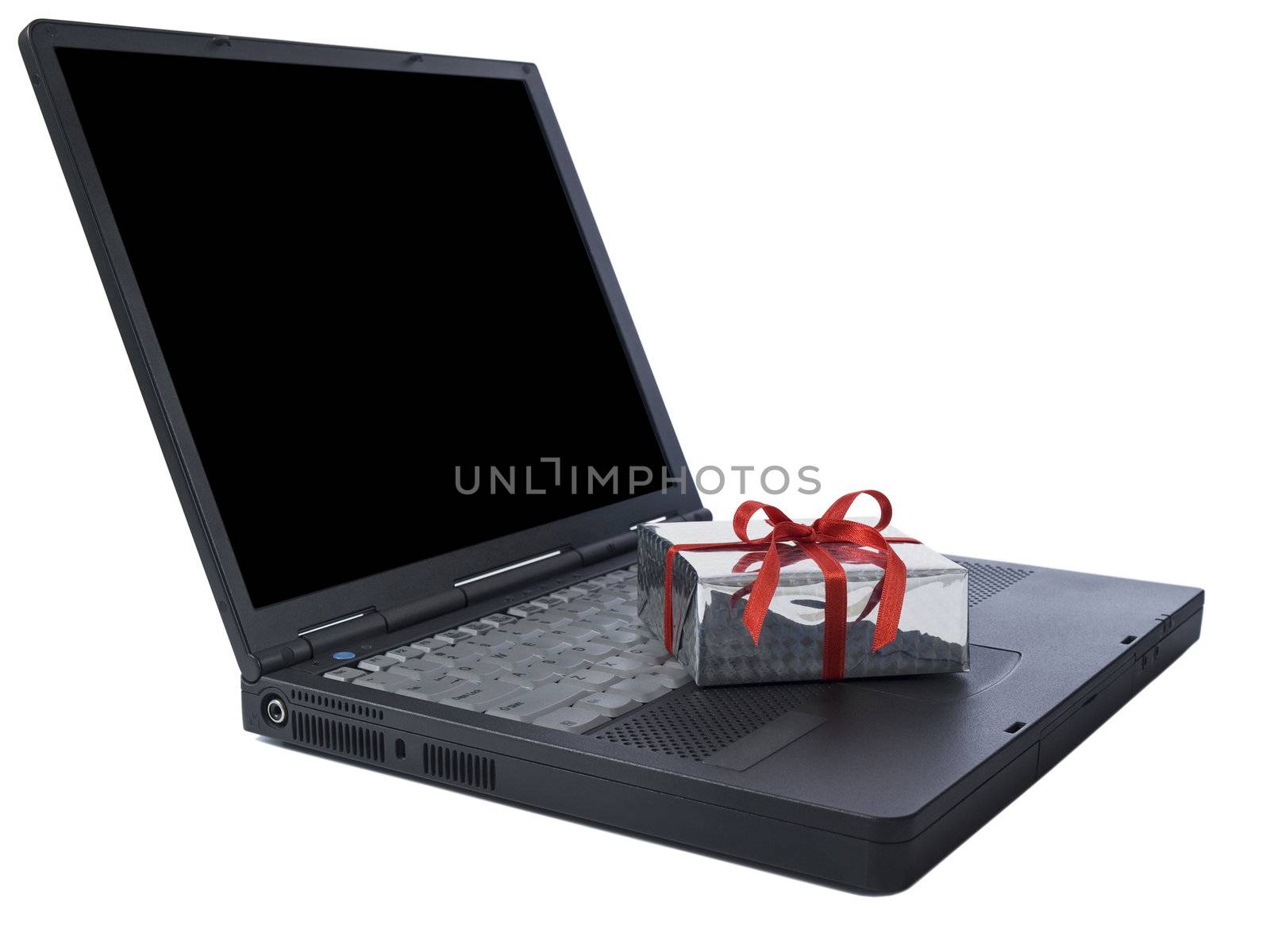 Small gift wrapped with a red ribbon over a black laptop isolated on white. Black copy space on screen.