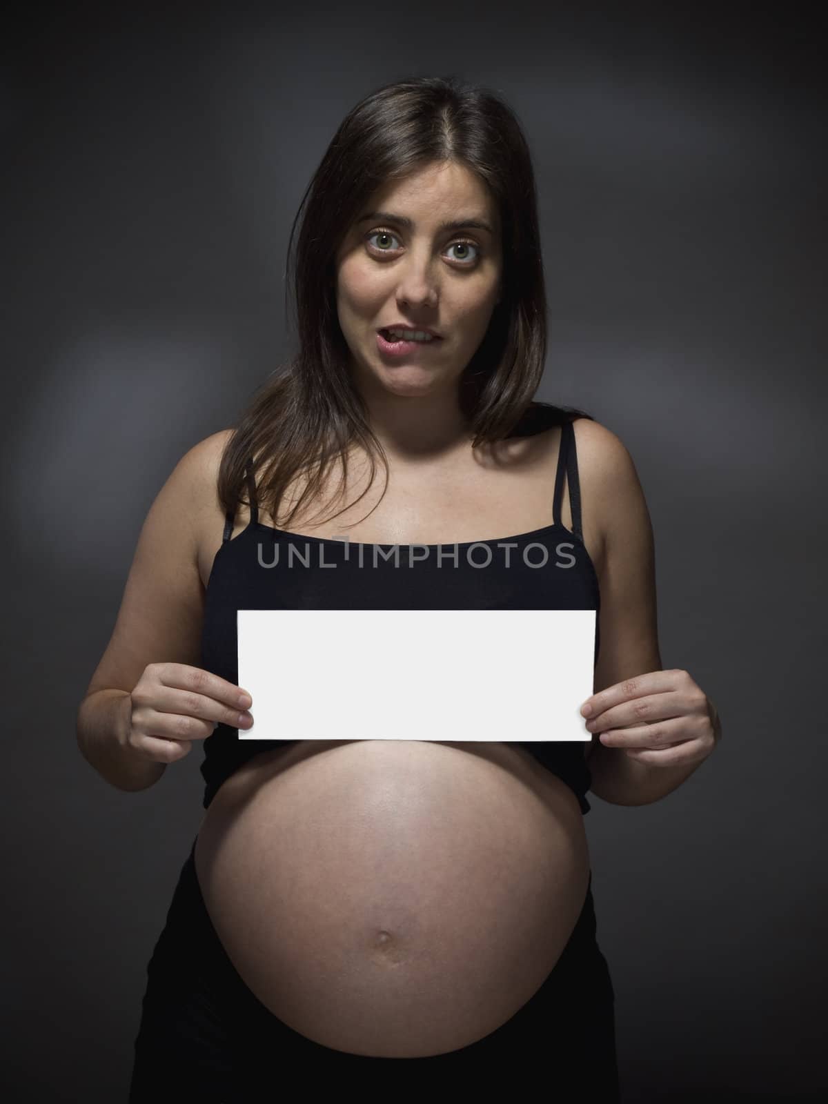 Pregnant woman holding a white card over gray background.