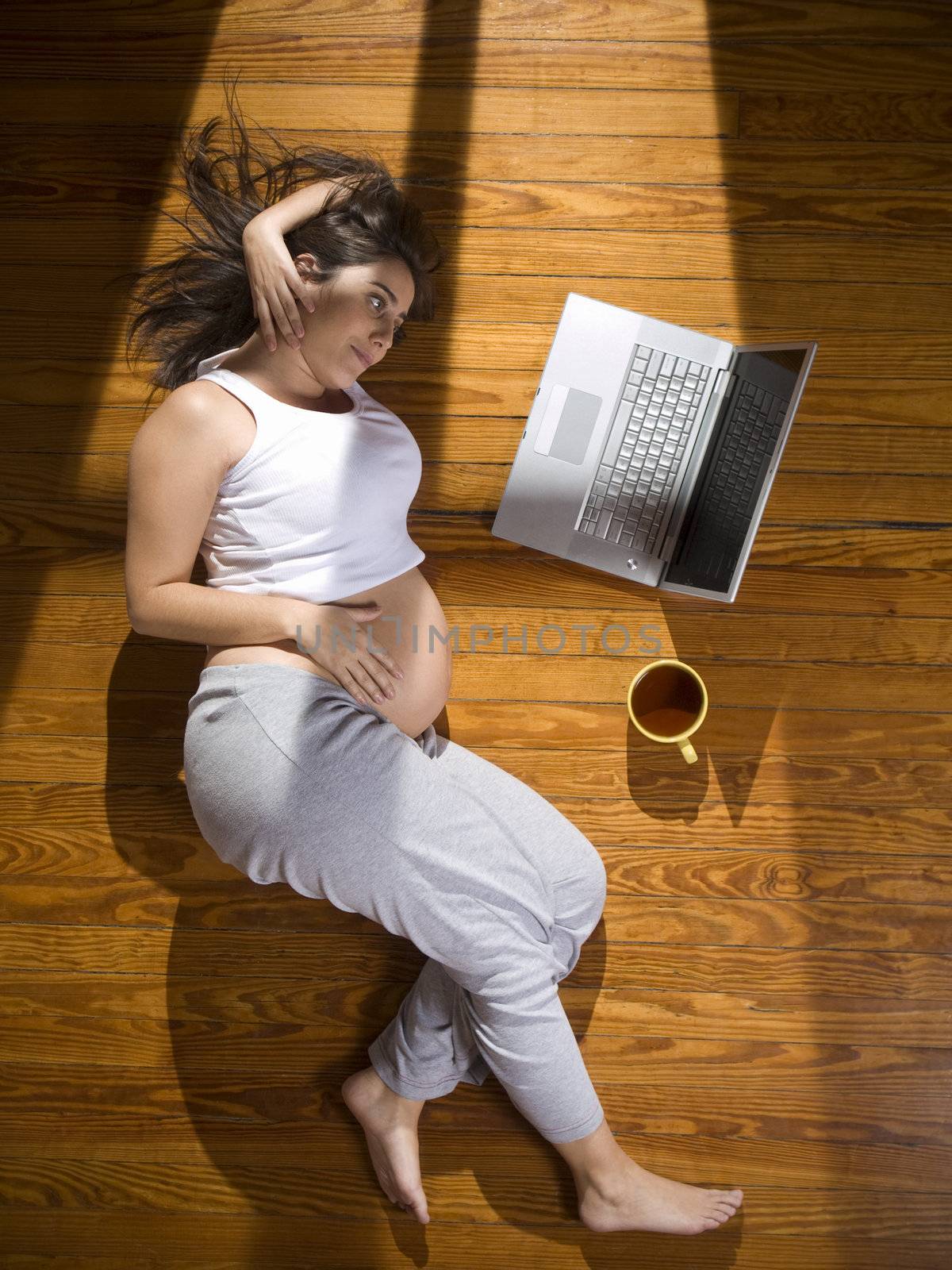 Top view of a young pregnant woman lying on the floor with a laptop computer and a cup of tea.