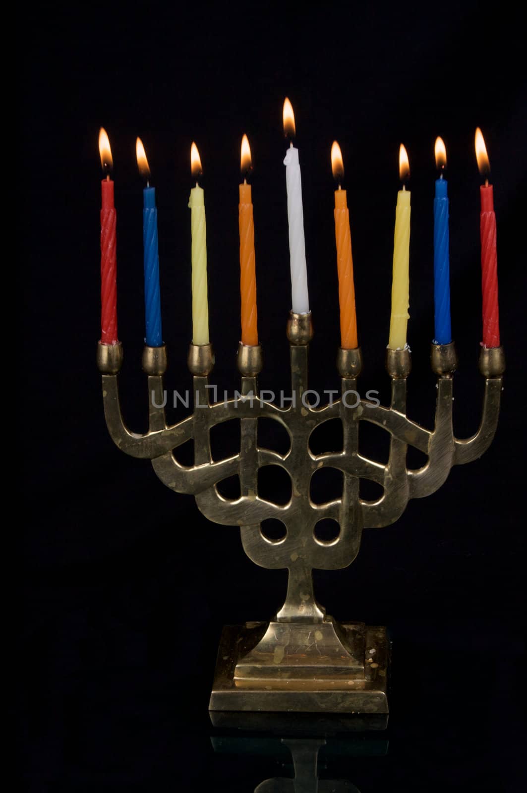 A gold colored menorak with lit Hanukah candles, isolated on black