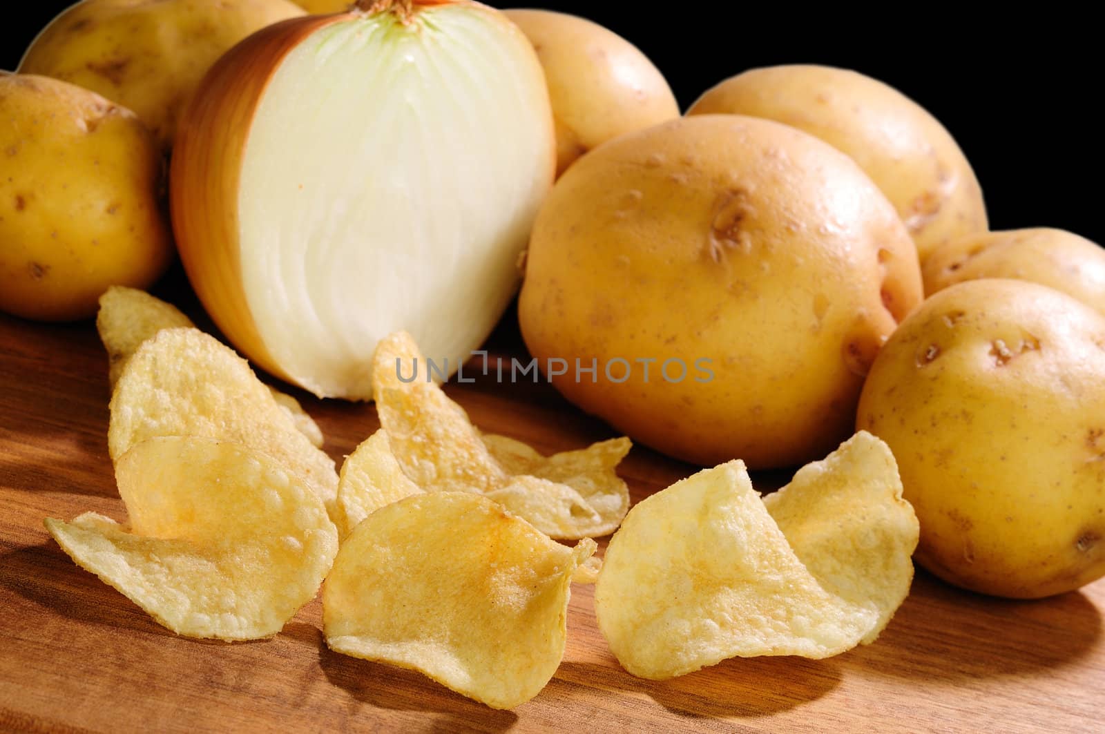 Onion flavored extra crispy potato chips with potatoes and onions in the background over black