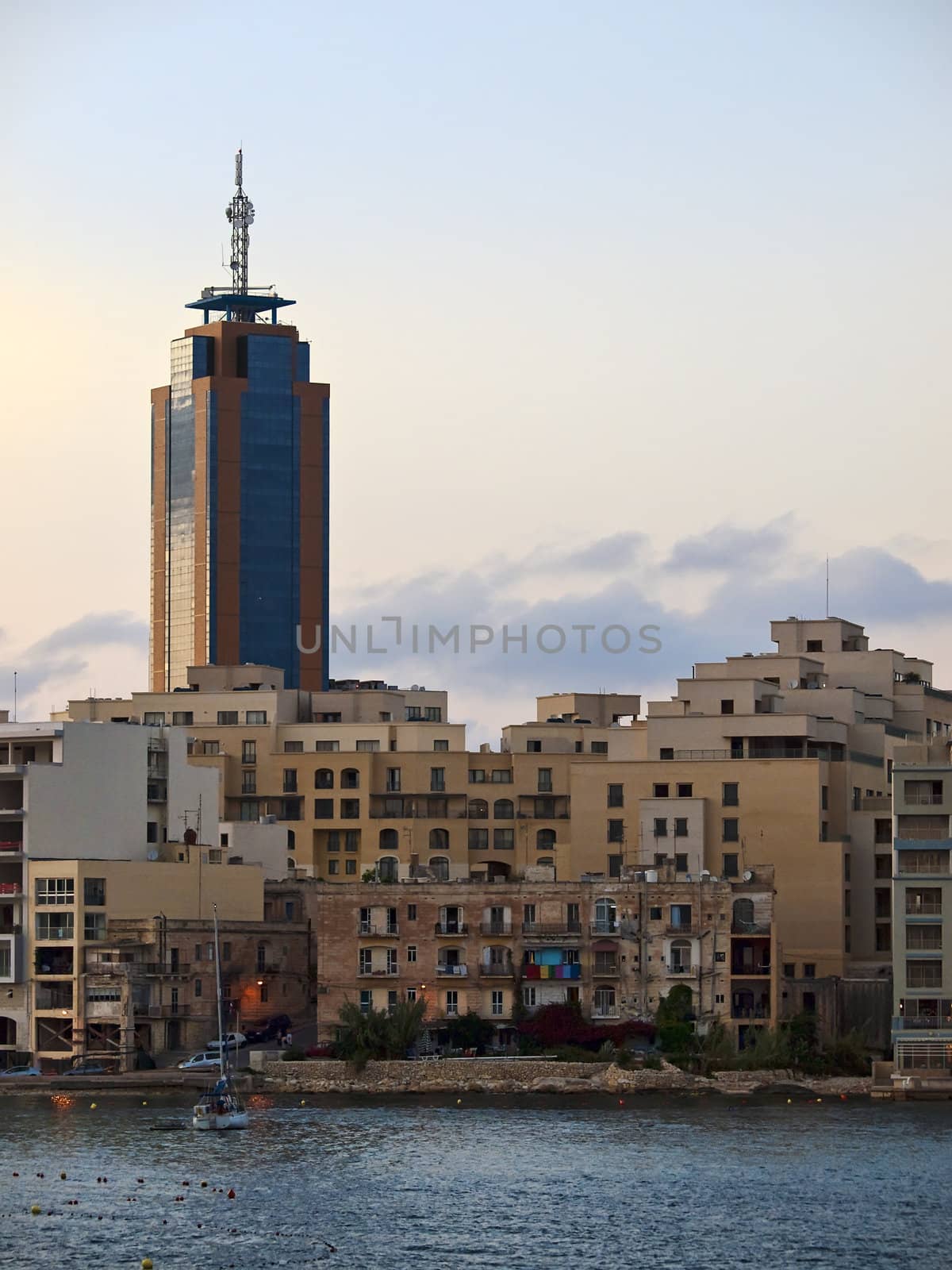 Old block of apartments on the seafront in Malta overshadowed by a modern skyscraper in the background